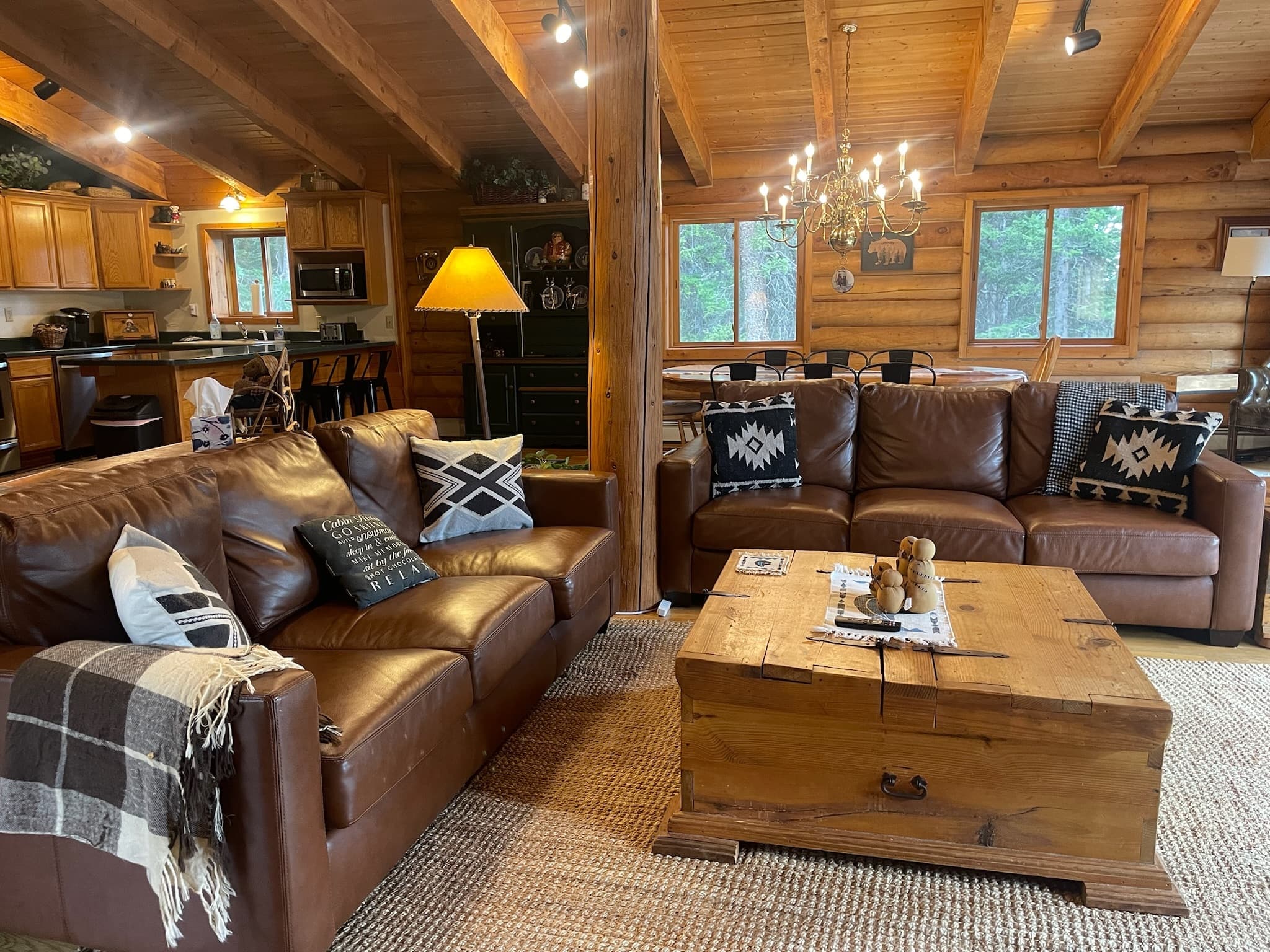 Rustic log cabin living room with leather sofas, wooden trunk coffee table, and warm lighting.