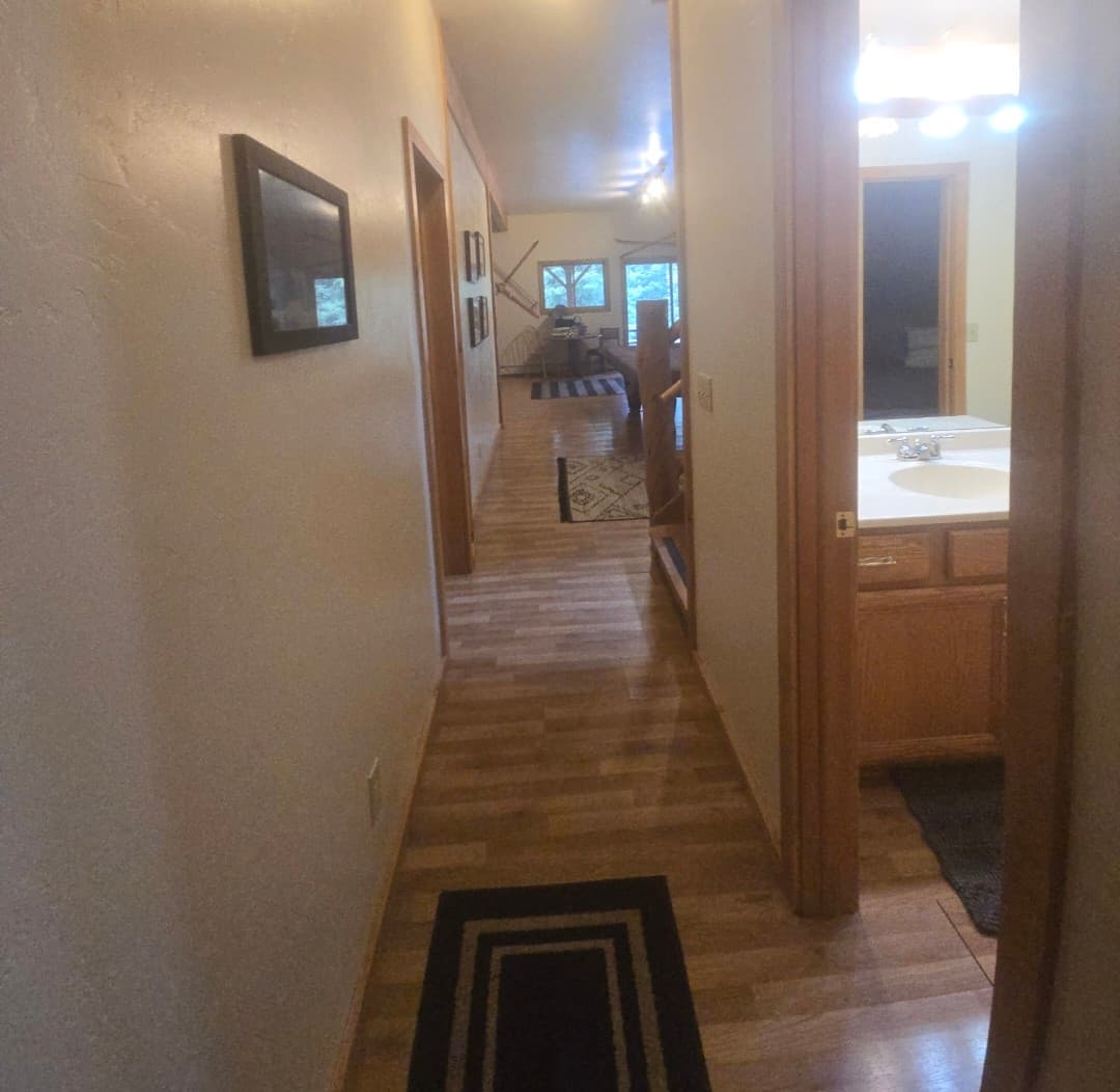 Long hallway with wood floors, framed art, and an open bathroom door on the right.