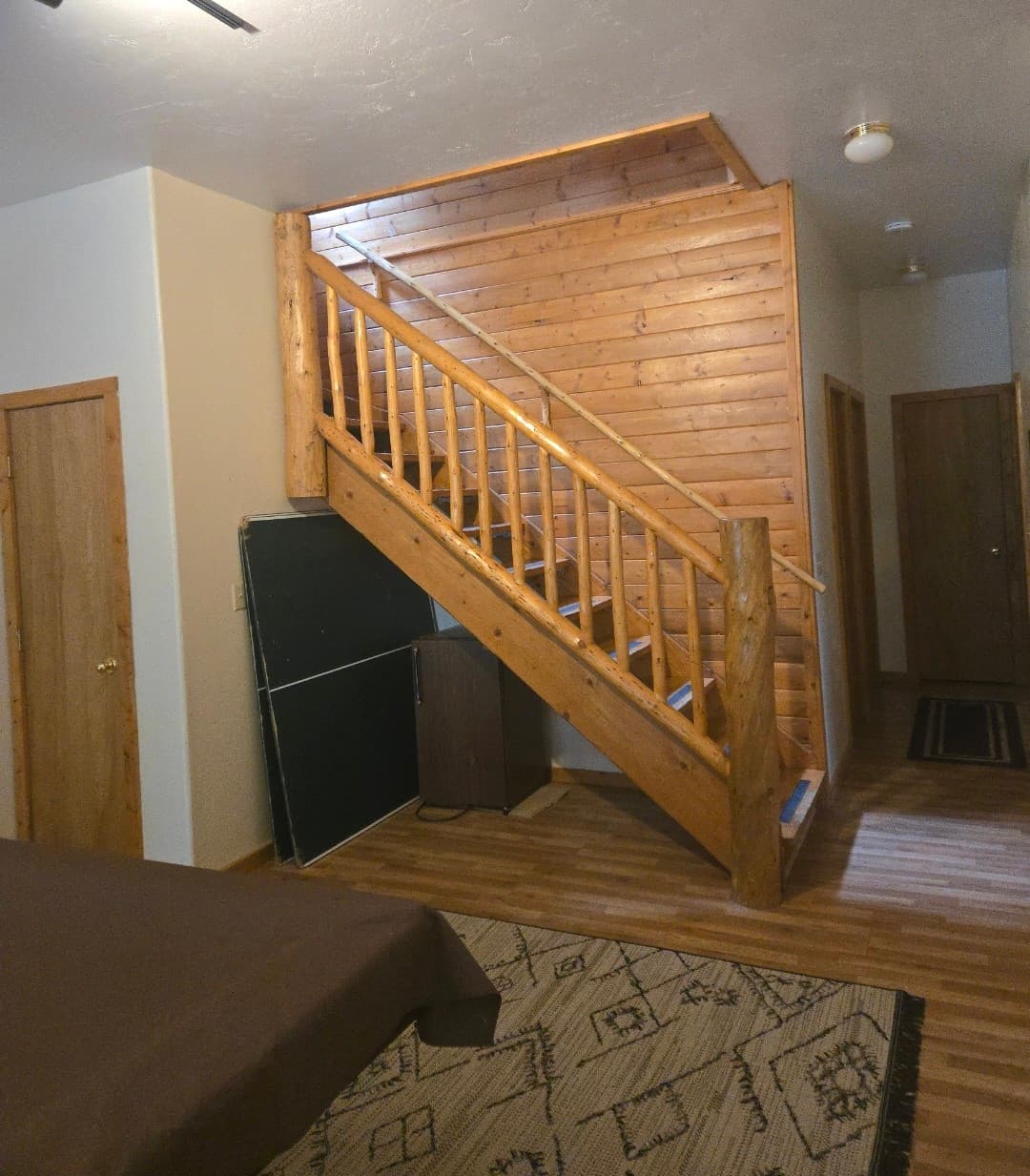 Rustic wooden staircase with log railings and banisters set against a light wood-paneled wall.