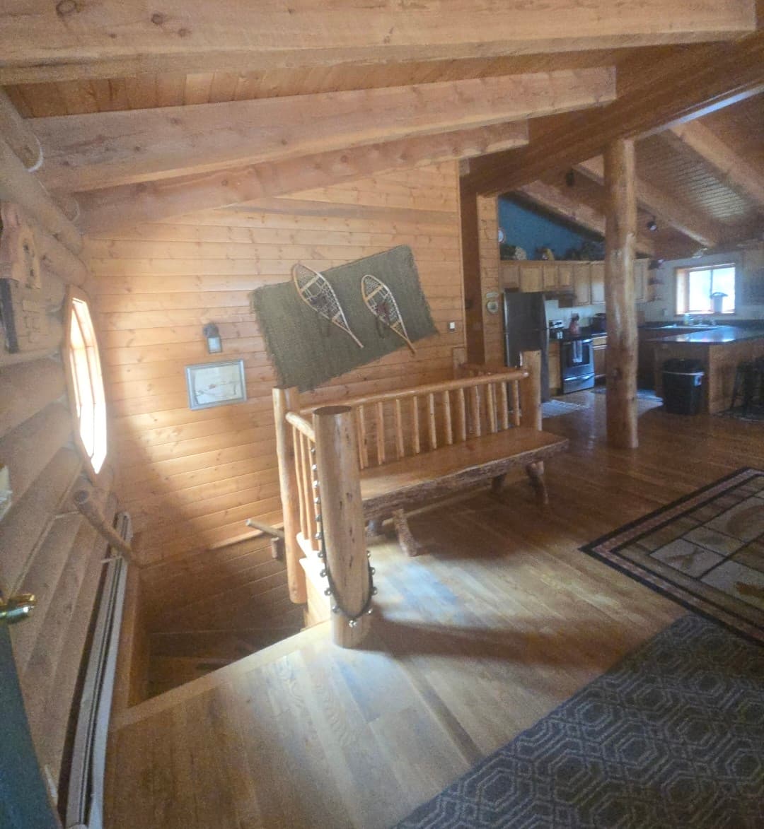 Rustic log cabin interior featuring a wooden bench, wall-mounted snowshoes, and a nearby staircase.