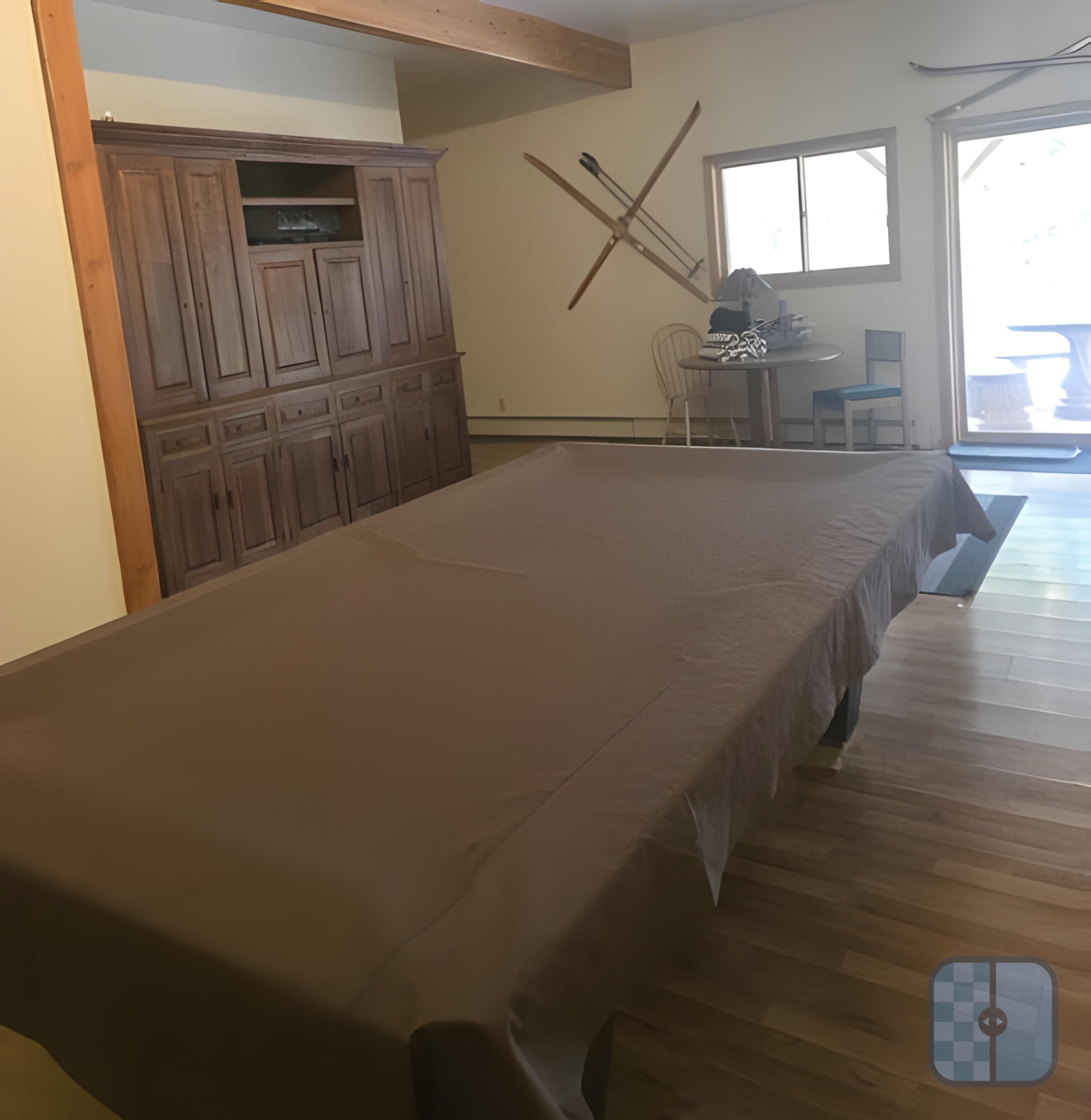 Pool table covered in brown cloth in a room with a wooden cabinet and skis.