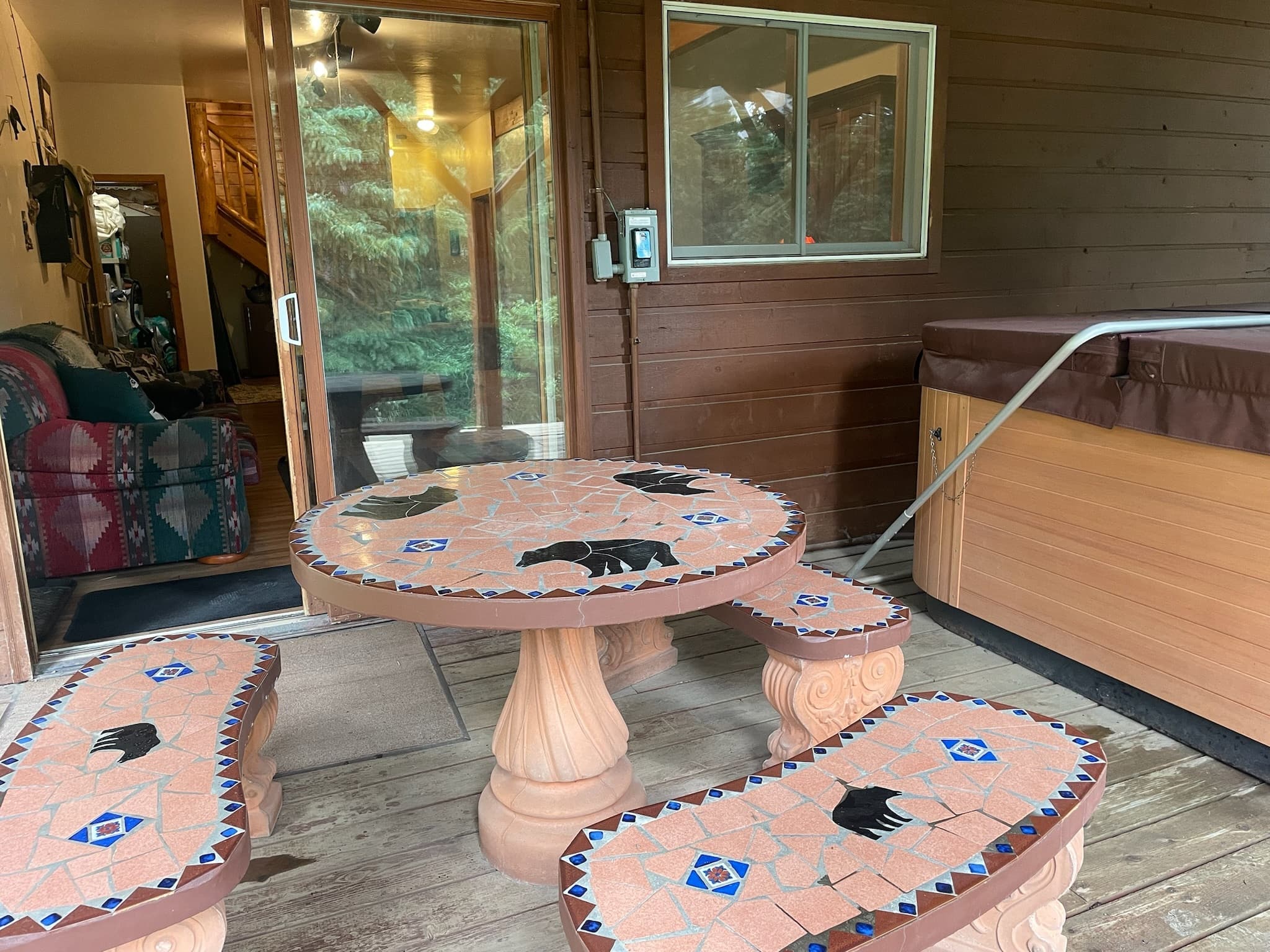 Stone mosaic table and benches with bear silhouettes on wooden deck beside a hot tub.