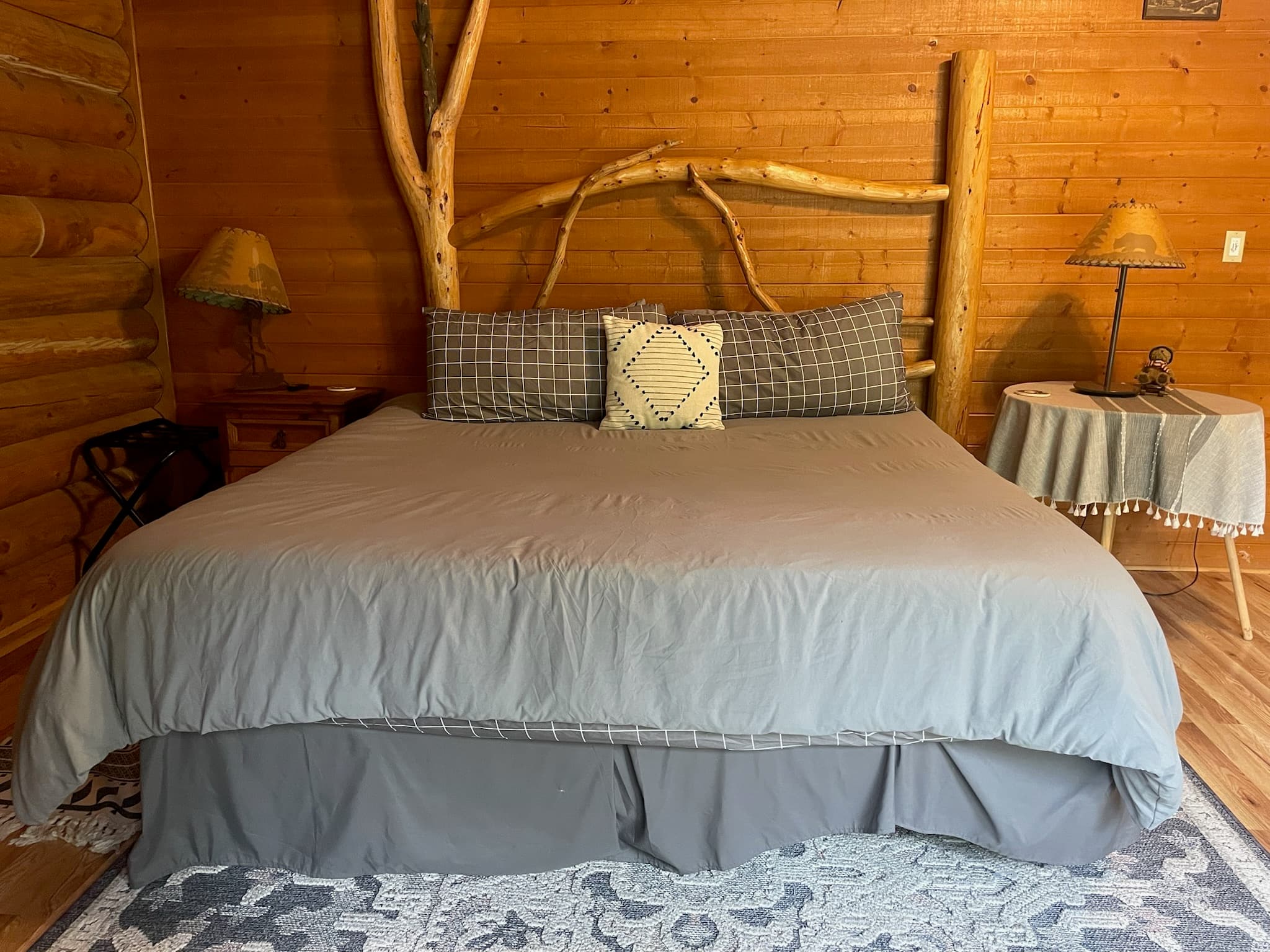 Rustic log cabin bedroom with a unique natural branch headboard and grey bedding.