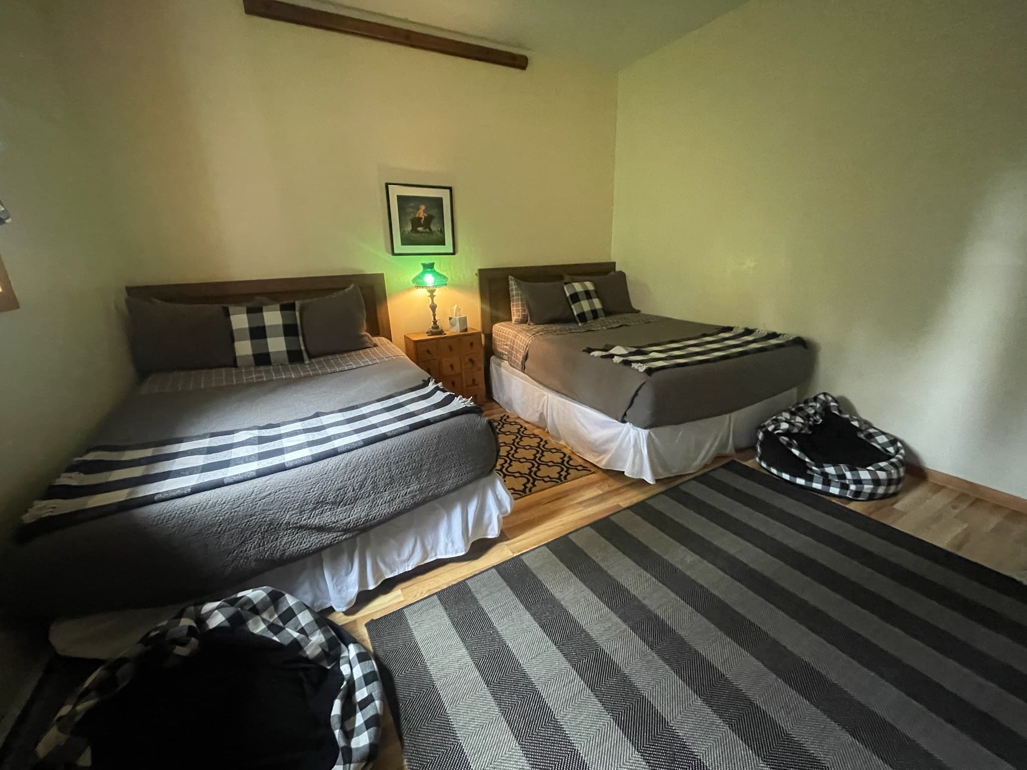 Two beds with grey and checkered bedding, a nightstand, and a large striped rug.